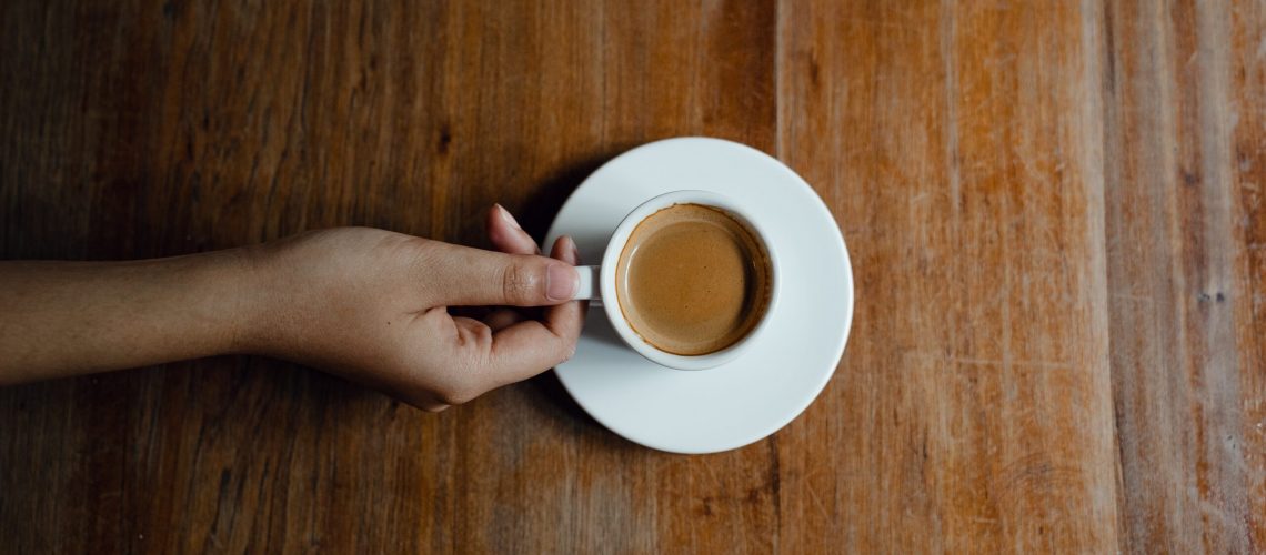 crop-person-with-cup-of-coffee-at-wooden-table-4350215